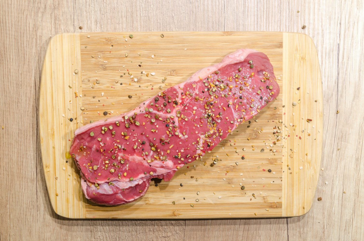 flat lay photography of slice of meat on top of chopping board sprinkled with ground peppercorns
